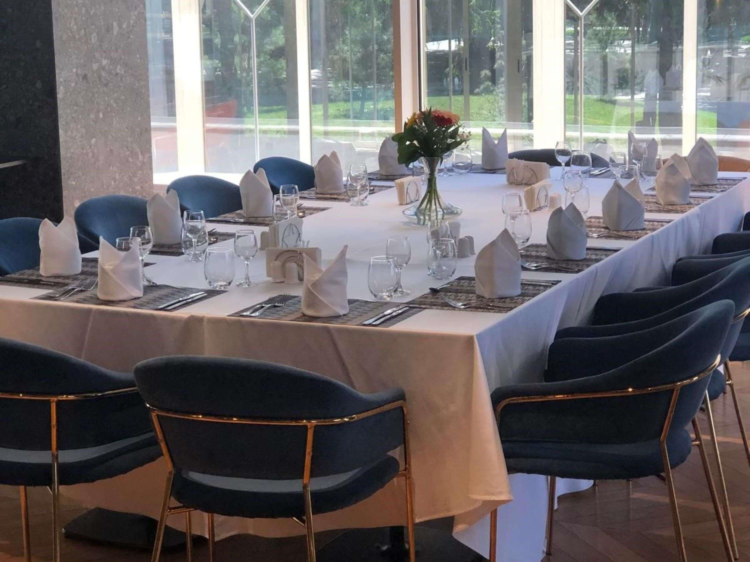 A long dining table set for a formal meal with blue chairs and a white tablecloth.