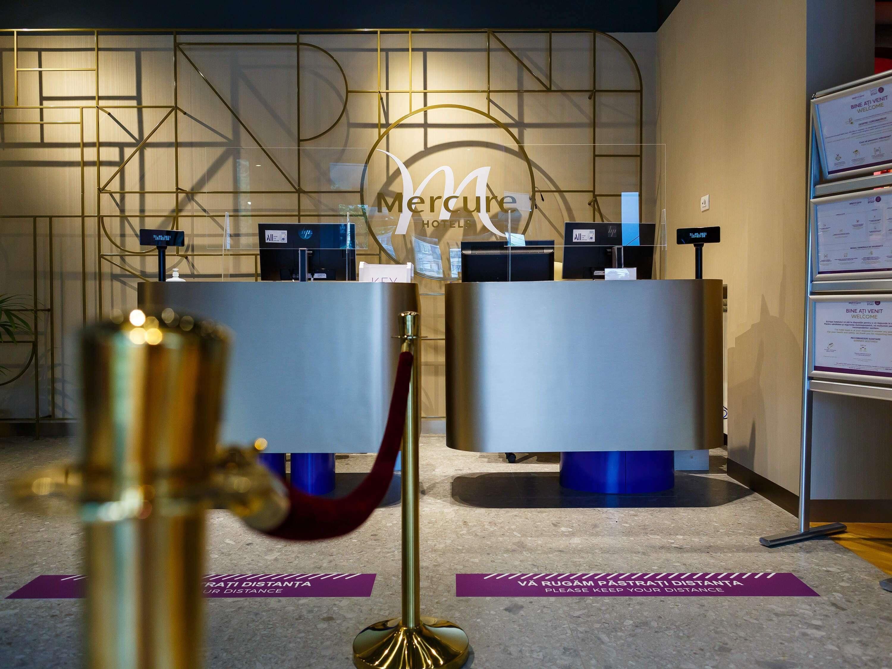 Una recepción con un logotipo, una alfombra azul con señalización que indica 'VA RUGAM PASTRATI DISTANTA' y un cartel que dice 'BINE ATI VENTI WELCOME'.