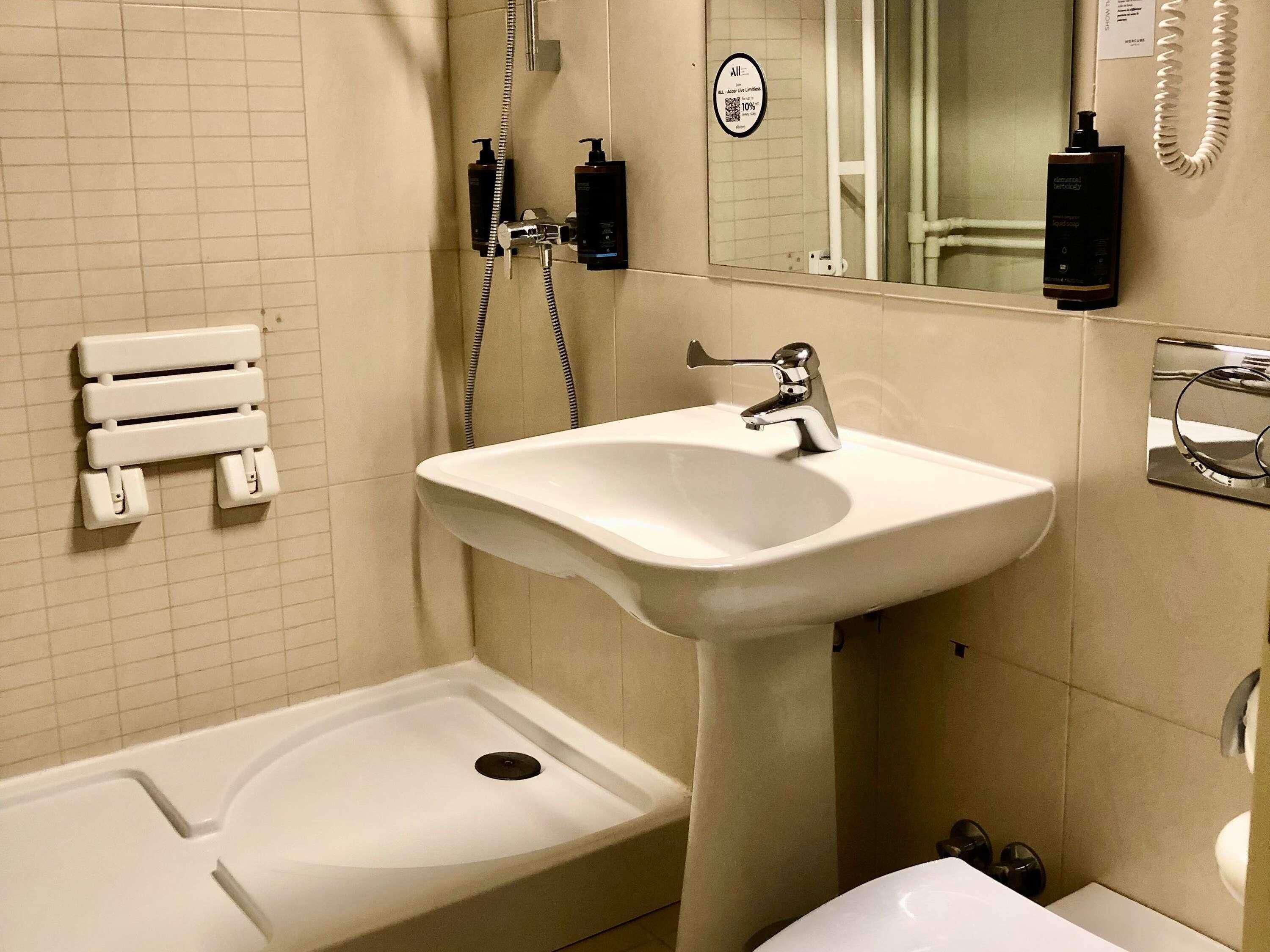 Ein Badezimmer mit einem weißen Waschbecken, einer Handbrause, einem Handtuchspender und einer Toilette.