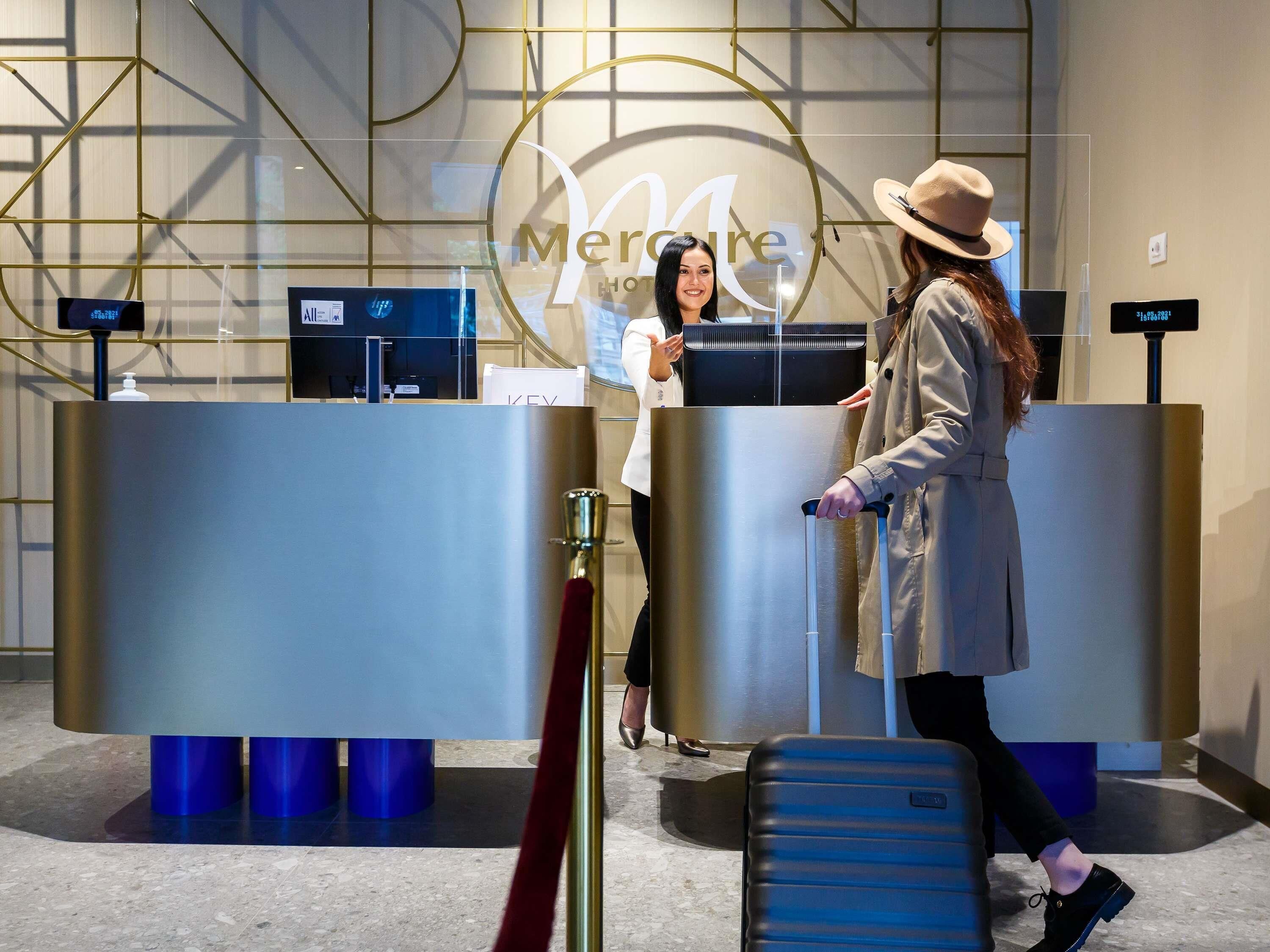 Un'area reception di un hotel dal design moderno, con una scrivania, un display digitale e un logo appeso al muro.