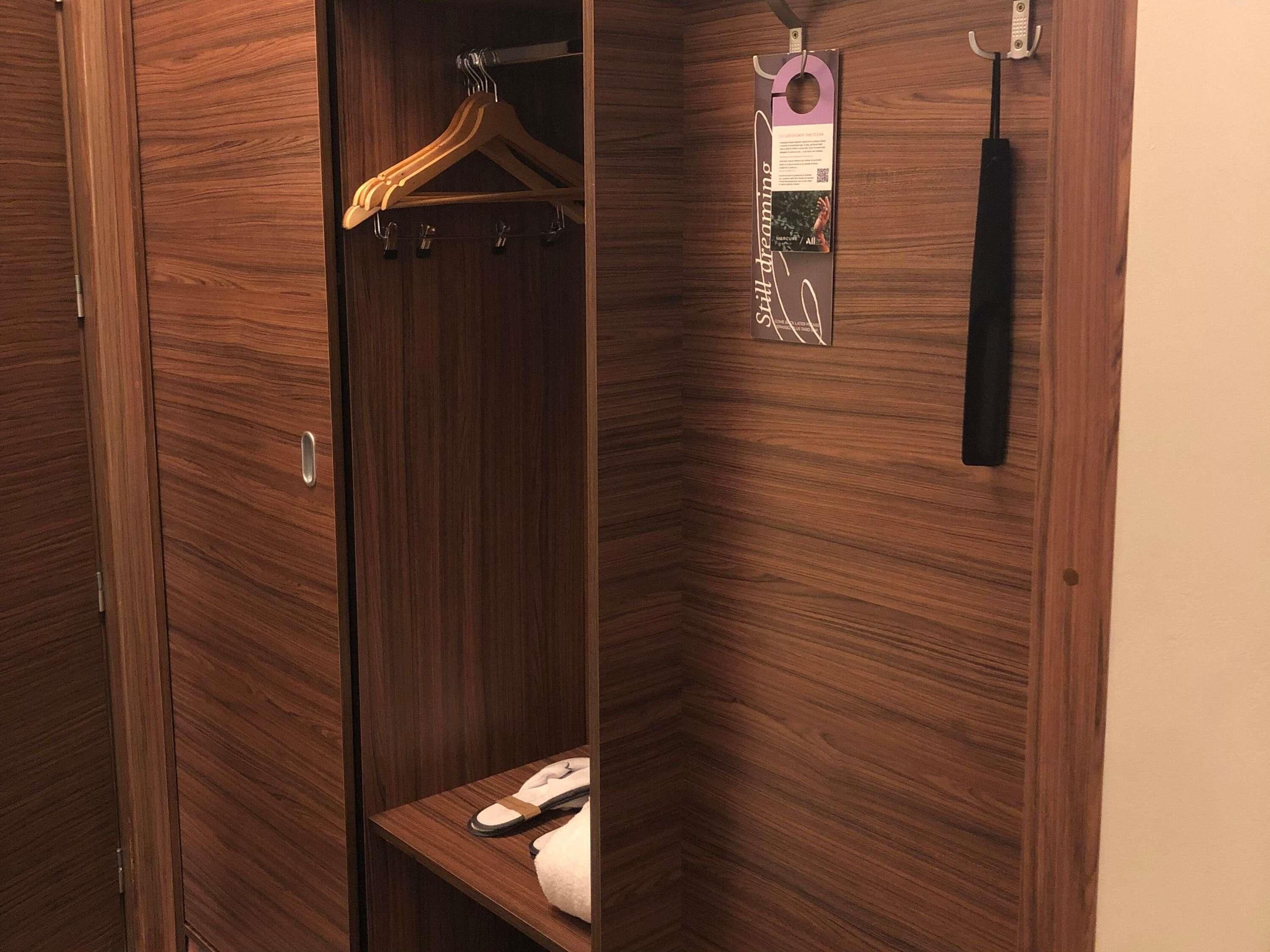 A wooden wardrobe with a hanging rack and a shelf with a phone and slippers.