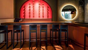 A bar area with a wooden counter, black bar stools, and a red wall with a geometric pattern. - Mercure Galati Centrum (Galati)