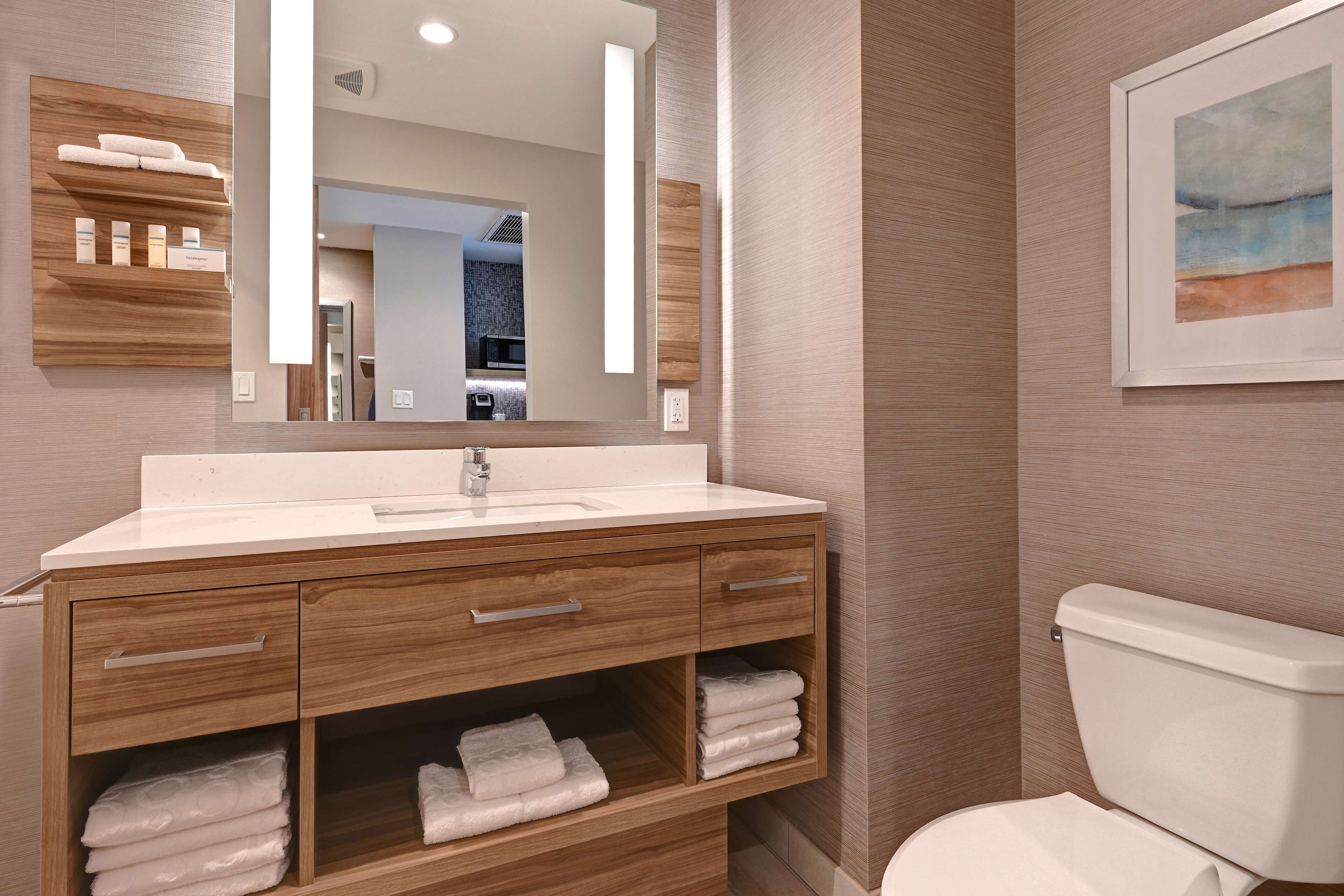 A modern bathroom with a wooden vanity, a large mirror, and a framed artwork on the wall.