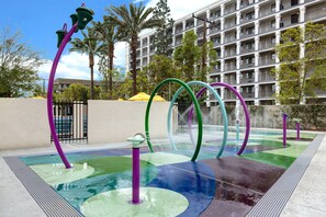 A water feature with colorful arches and a pool area, surrounded by palm trees and a hotel building in the background.