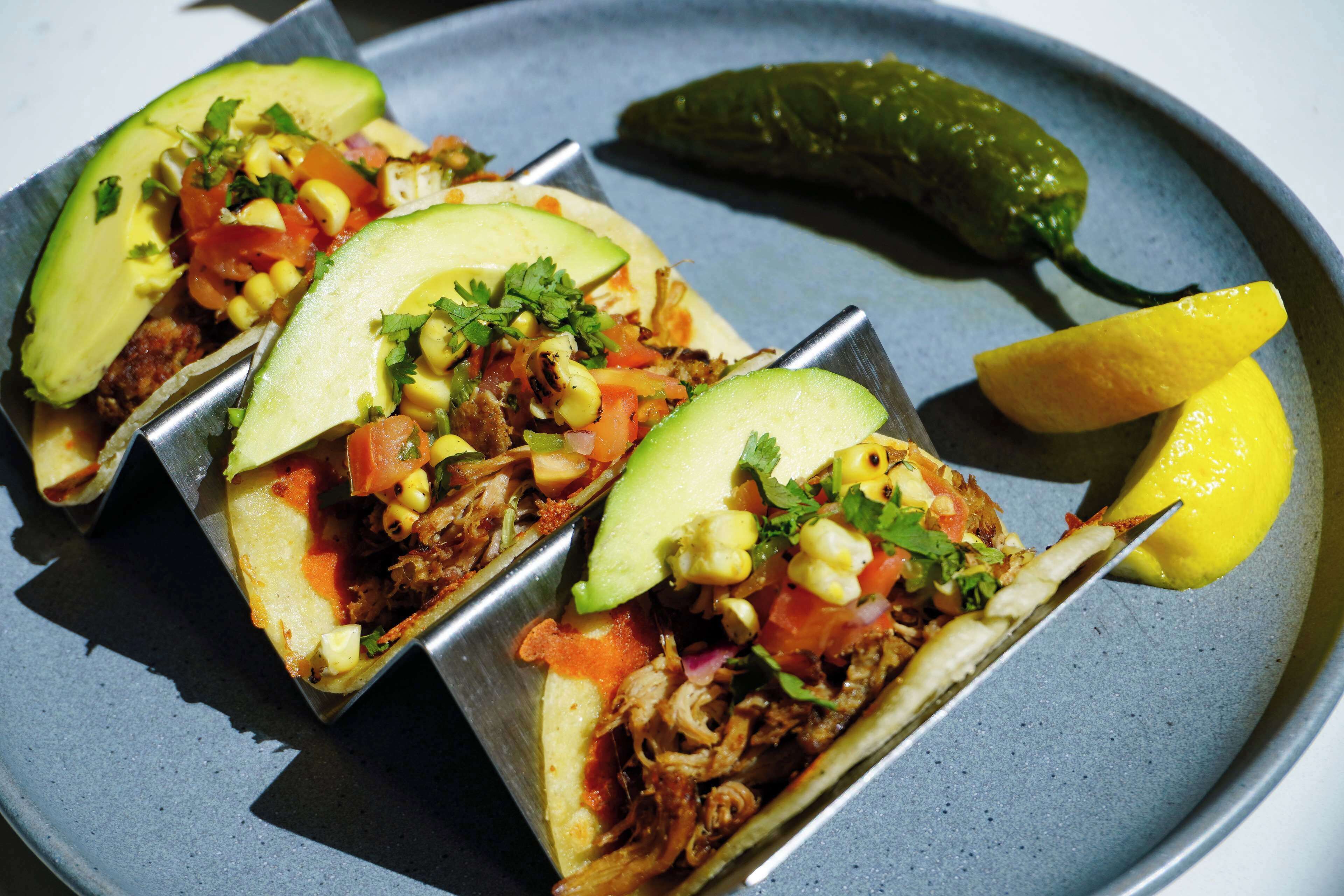Tres tacos con aguacate y elote en un plato.