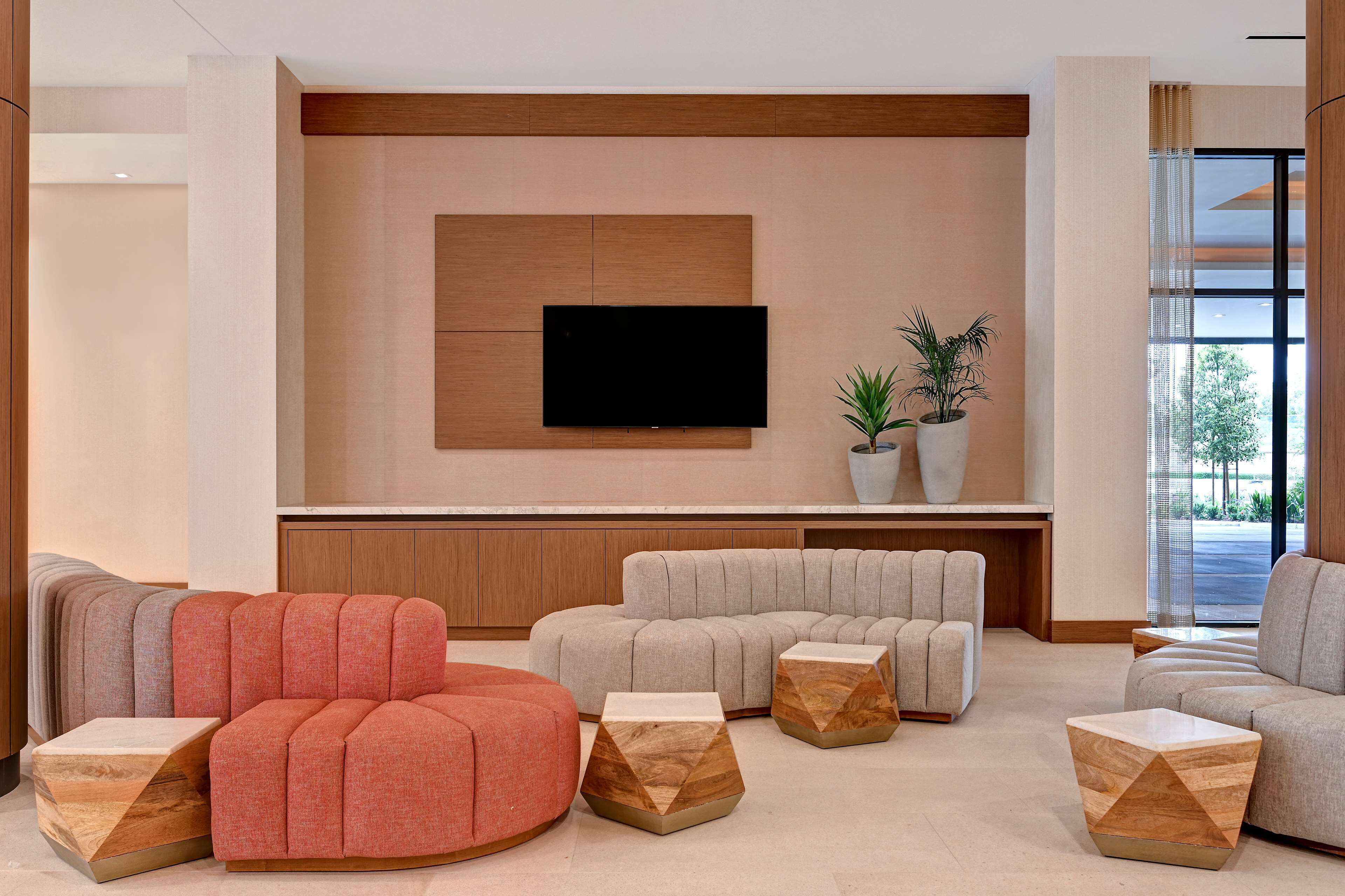 Un salon moderne avec un téléviseur à écran plat fixé à un mur en bois, entouré de canapés et de tables basses aux formes géométriques.