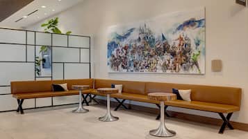 A modern lobby with a long bench, three round tables, and a large abstract painting on the wall.