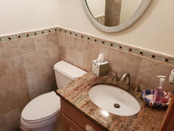 A bathroom with a white toilet, a granite countertop, a sink with a mirror above, and a decorative tile border.