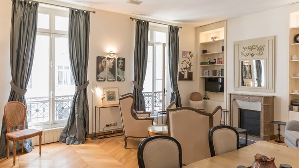 A cozy living room with a fireplace, a dining area, and a balcony with curtains. - Monceau Chic I Charming 1 Bed Apt in the 8th (Paris)
