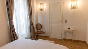 A hotel room with a bed, a chair, a door, and wall-mounted lights. - Monceau Chic I Charming 1 Bed Apt in the 8th (Paris)