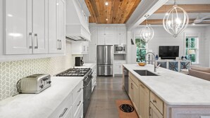 A modern kitchen with white cabinets, stainless steel appliances, and a wooden ceiling.