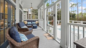 A covered porch with wicker furniture and a view of the pool.