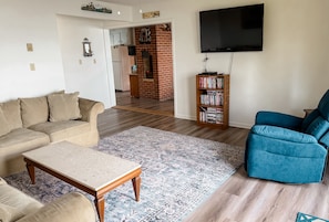 Un salón con sofá, mesa de centro, sillón azul, estantería y televisor montado en la pared.