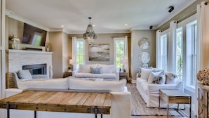 A spacious living room with a fireplace, a large wooden table, and two white sofas.