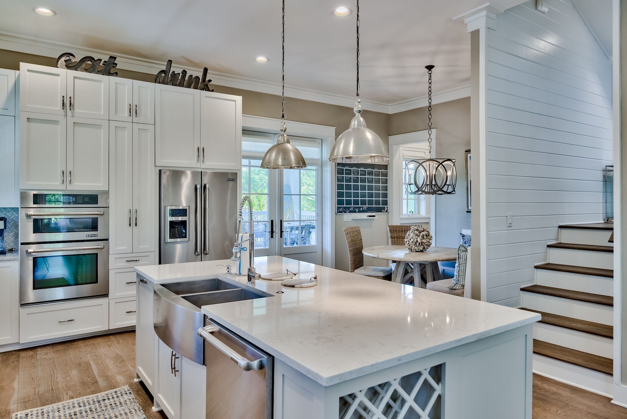 A modern kitchen with white cabinetry, stainless steel appliances, and pendant lighting.