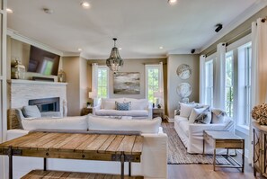 A spacious living room with a fireplace, a large wooden table, and two white sofas.