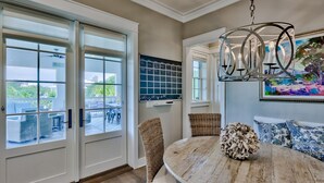 A dining area with a round wooden table, wicker chairs, a chandelier, and a view through glass doors to an outdoor patio.