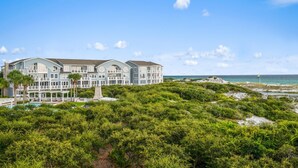 Un hotel grande de varios pisos frente a la playa, con piscina y zona de estar al aire libre.
