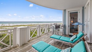 Una terraza de madera con dos sillones y una mesa, con vista a la playa.