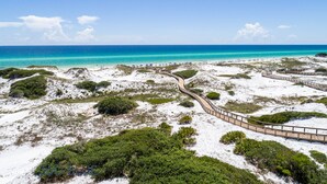 Una playa con un paseo marítimo de madera, dunas de arena y vegetación escasa.