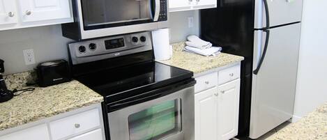 Una cocina con armarios blancos, un refrigerador de acero inoxidable, un microondas, un tostador y un horno.