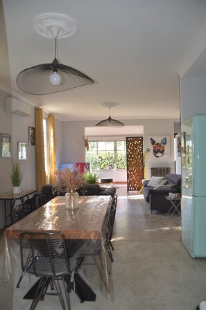 A dining area with a table, chairs, and pendant lights. There is a sofa and a refrigerator in the background. - Villa, 300 metres from the beaches of Juan les Pins with heated swimming pool (Antibes)