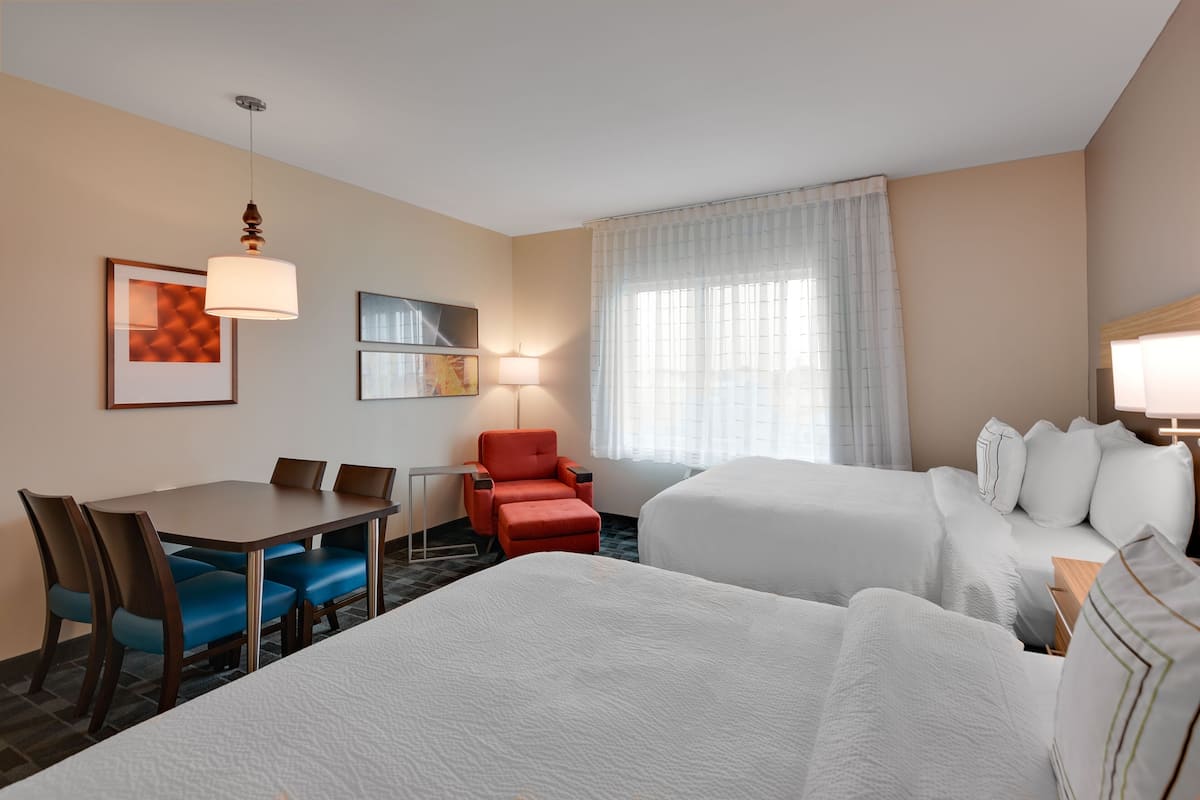Une chambre d’hôtel avec un lit, un bureau avec des chaises, un fauteuil rouge et une lampe.