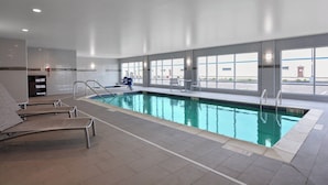 An indoor swimming pool with clear water, a tiled floor, and a view of the outside through large windows.