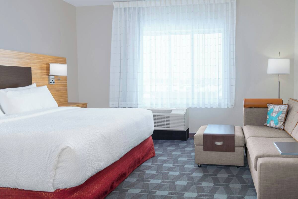 Une chambre d’hôtel avec un grand lit, un canapé, un bureau et une fenêtre avec des rideaux légers.