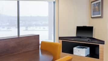 Une chambre d’hôtel moderne avec une grande fenêtre, un bureau équipé d’un ordinateur et d’une imprimante, ainsi qu’une chaise jaune.