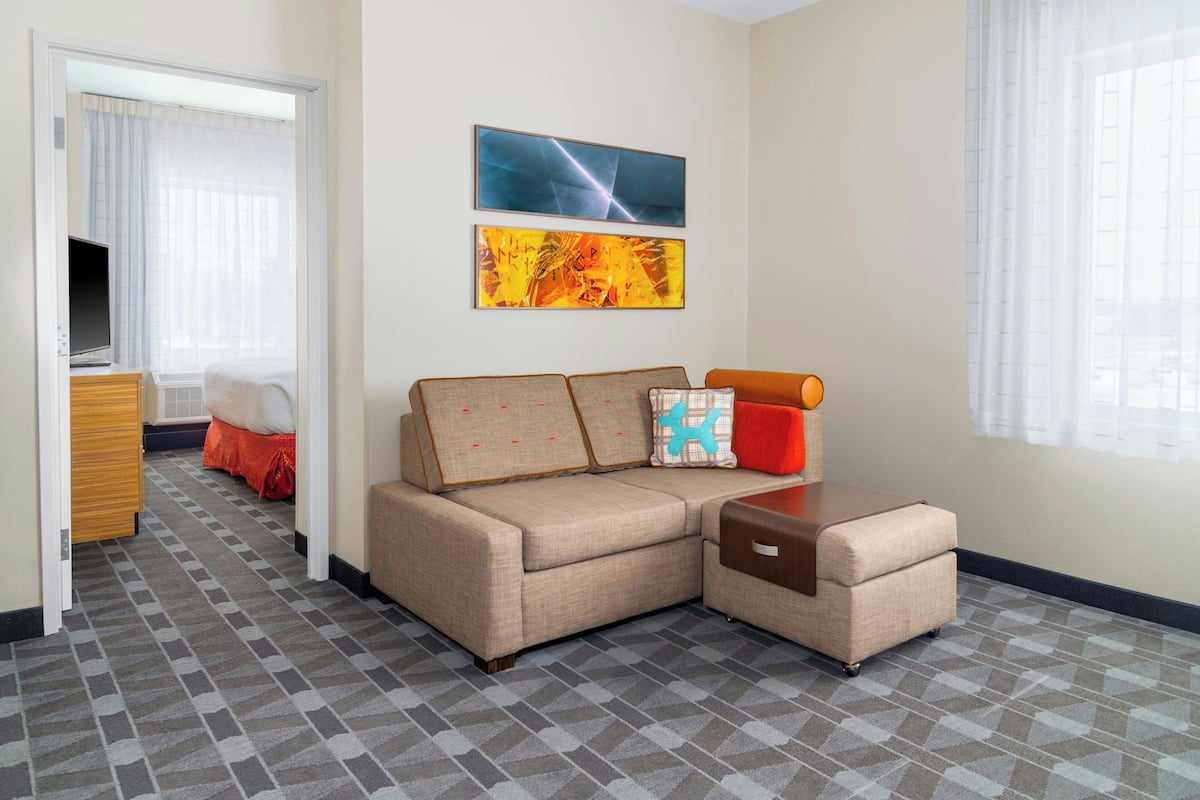 Une chambre d’hôtel avec un canapé, un pouf et une télévision.