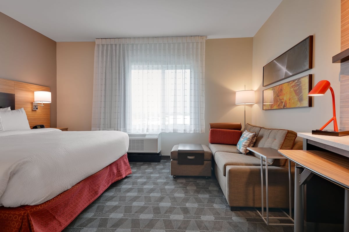 Une chambre d’hôtel avec un grand lit, un bureau, un canapé, une petite table et une fenêtre avec des rideaux.