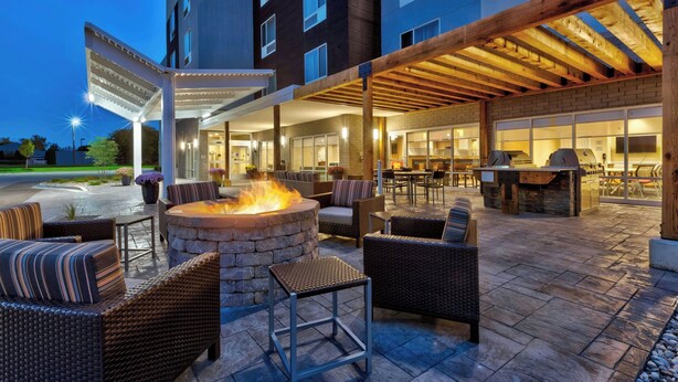 An outdoor patio area with wicker furniture, a stone fire pit, and a grill.