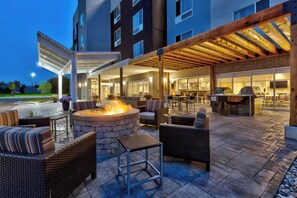 An outdoor patio area with wicker furniture, a stone fire pit, and a grill. - TownePlace Suites by Marriott Grand Rapids Airport Southeast (Grand Rapids)