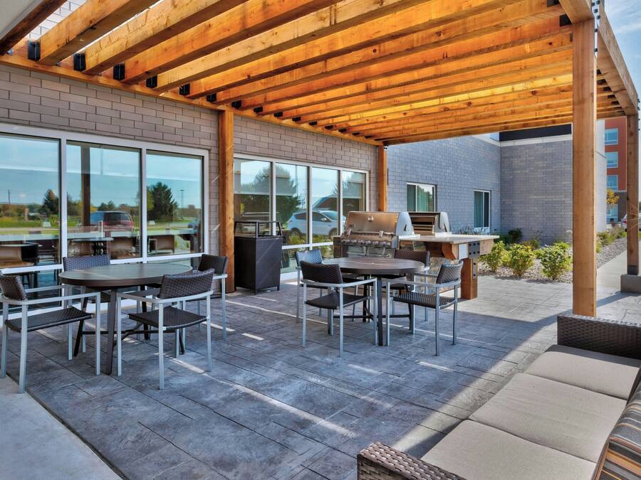 An outdoor patio with a wooden pergola, a barbecue grill, and a seating area with tables and chairs.