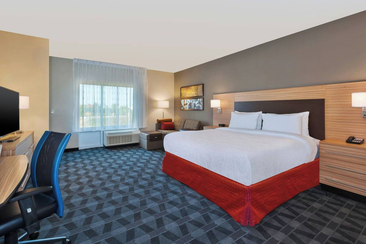Una habitación de hotel con cama, escritorio, silla y ventana con cortinas.