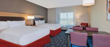 A hotel room with two beds, a desk, chairs, a lamp, and a window with curtains.