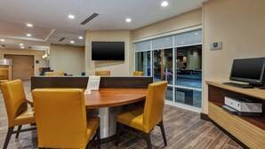 A conference room with a round table, yellow chairs, a flat-screen TV, and a glass door leading outside.