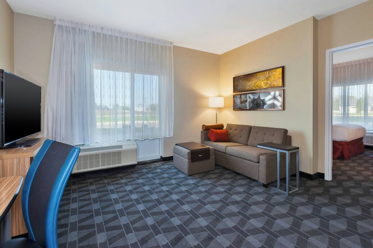 Habitación de hotel con televisión de pantalla plana, un sofá, escritorio, silla, lámpara y un cuadro en la pared.