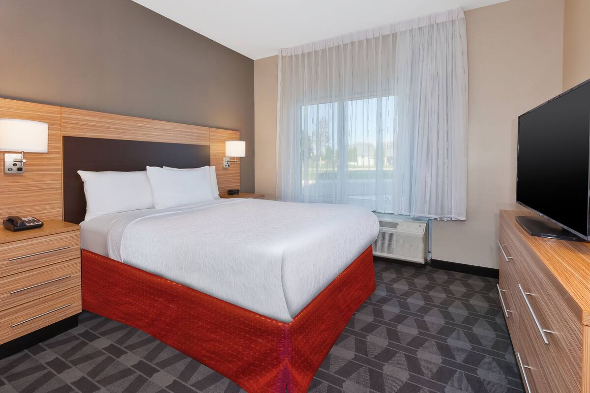 Una habitación de hotel con una cama grande, mesitas de noche, un televisor y un ventanal con cortinas.