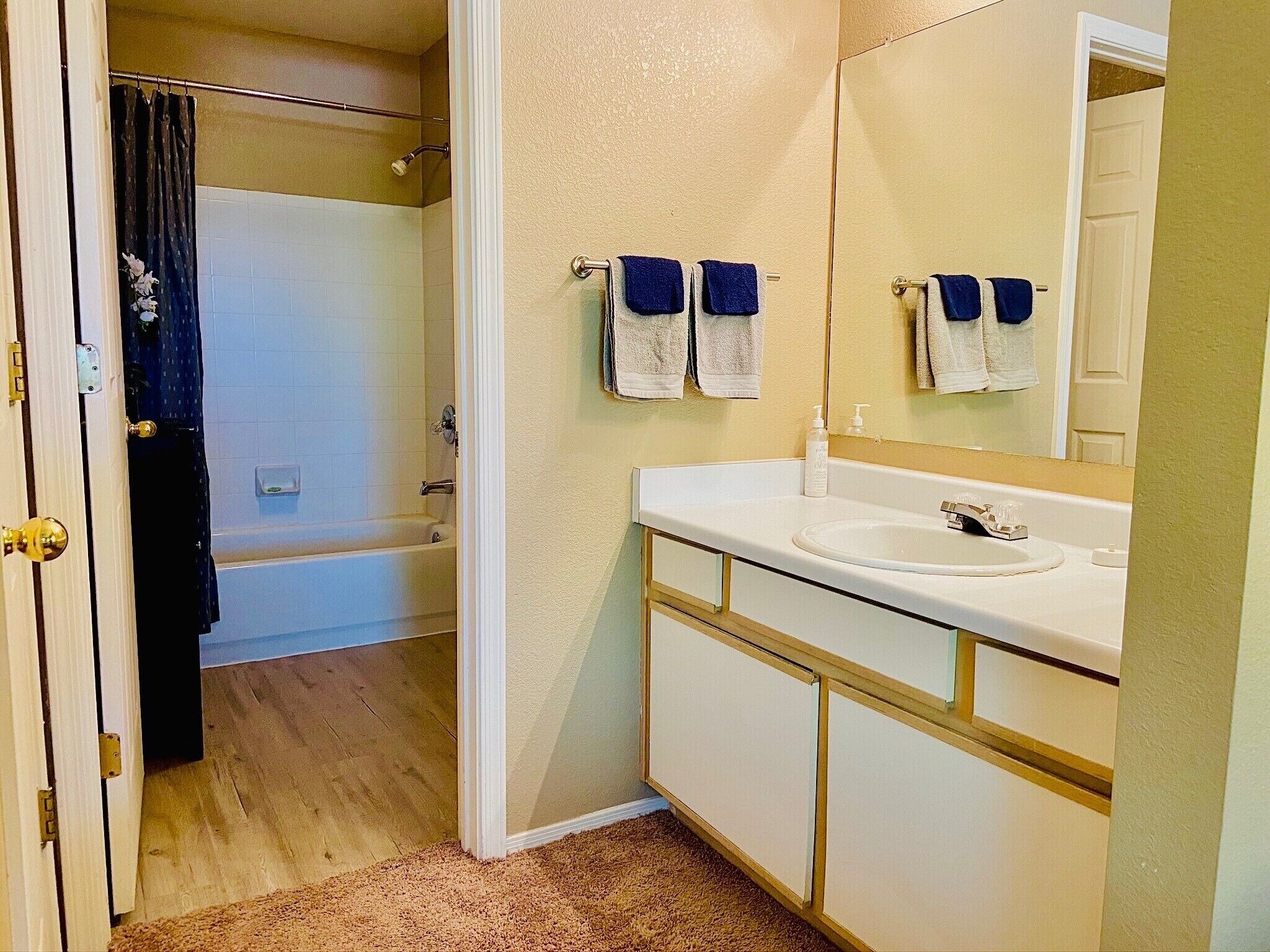 A bathroom with a white sink, a mirror, and a shower. There are towels hanging on the wall.