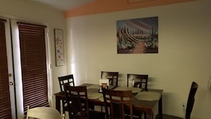 Un comedor con una mesa y sillas, un cuadro en la pared y una puerta con persianas.