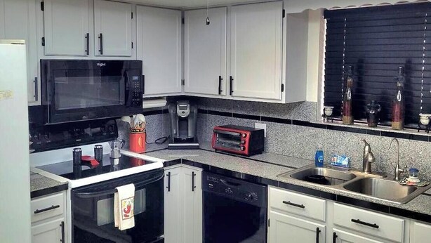 Una cocina moderna con armarios blancos, un microondas negro, un tostador rojo, lavavajillas y un ventilador de techo.