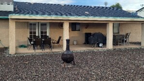 Una casa con un patio cubierto, zona de barbacoa y un pájaro en el suelo.