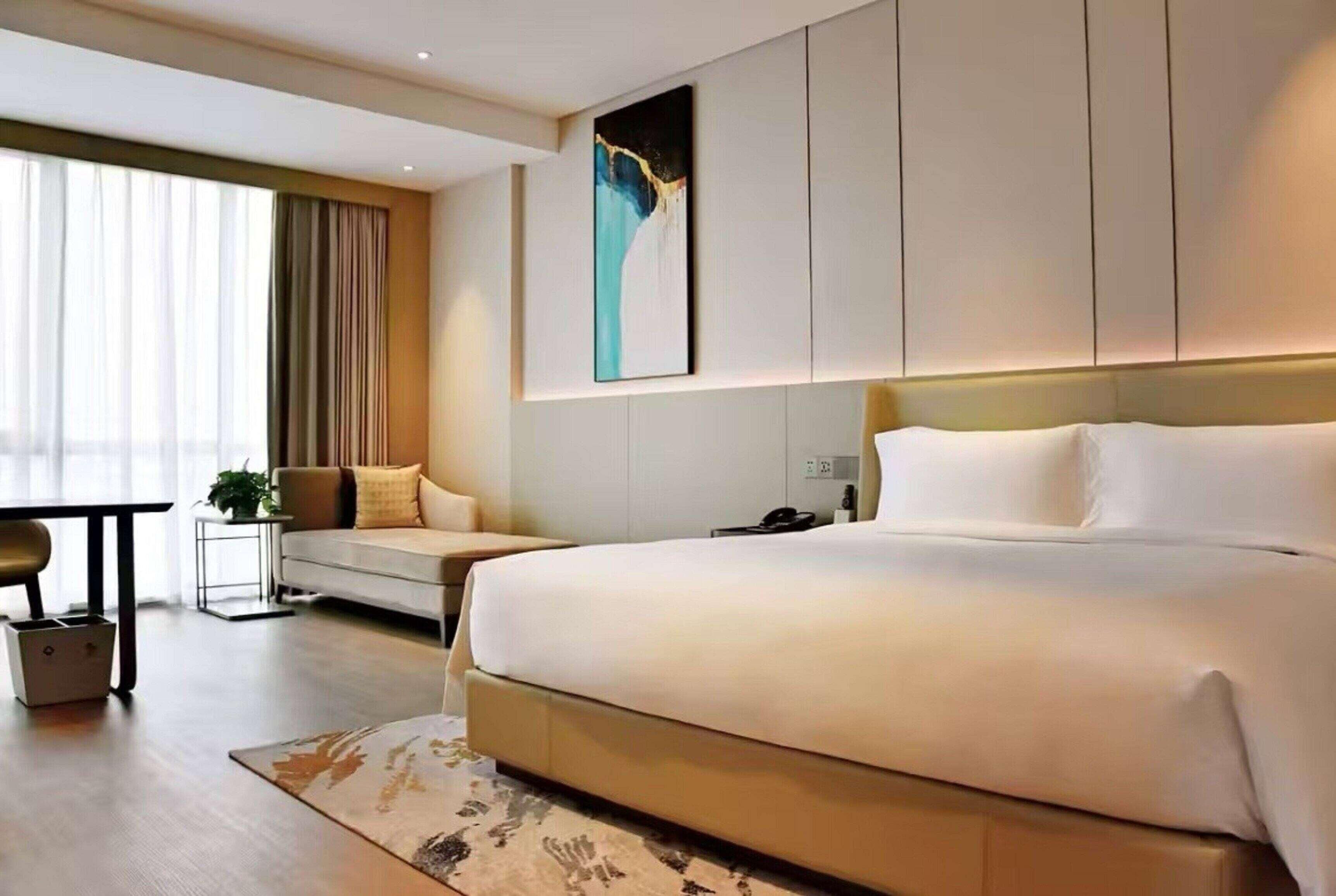Quarto de hotel moderno com uma cama grande, um sofá, uma escrivaninha e um quadro na parede.