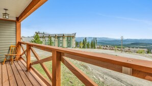 Una terraza de madera con vistas a un edificio de varios pisos y montañas distantes.