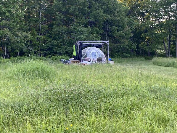 A dome tent set up in a grassy field with solar panels and camping chairs. - ComfyDome Forest-Side Glamping (Jefferson)