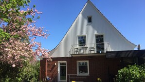 A two-story building with a white exterior and a brick base. There is a balcony with outdoor furniture on the upper floor. - Vacation apartment directly on the Ems dyke in an idyllic location (Westoverledingen)