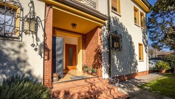 A two-story house with a brick facade, a wooden door, and a small porch with potted plants.