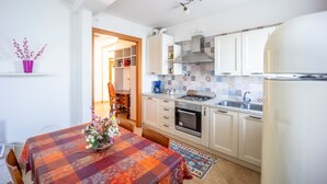 A compact kitchen with white cabinets, a gas stove, an oven, and a sink. There is a dining table with a colorful tablecloth and a vase of flowers.